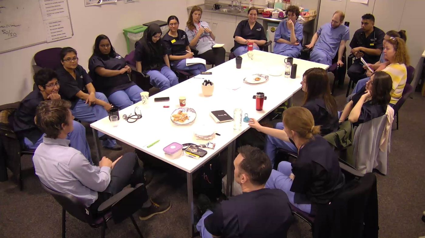Faculty and delegates in a debrief discussion around a table