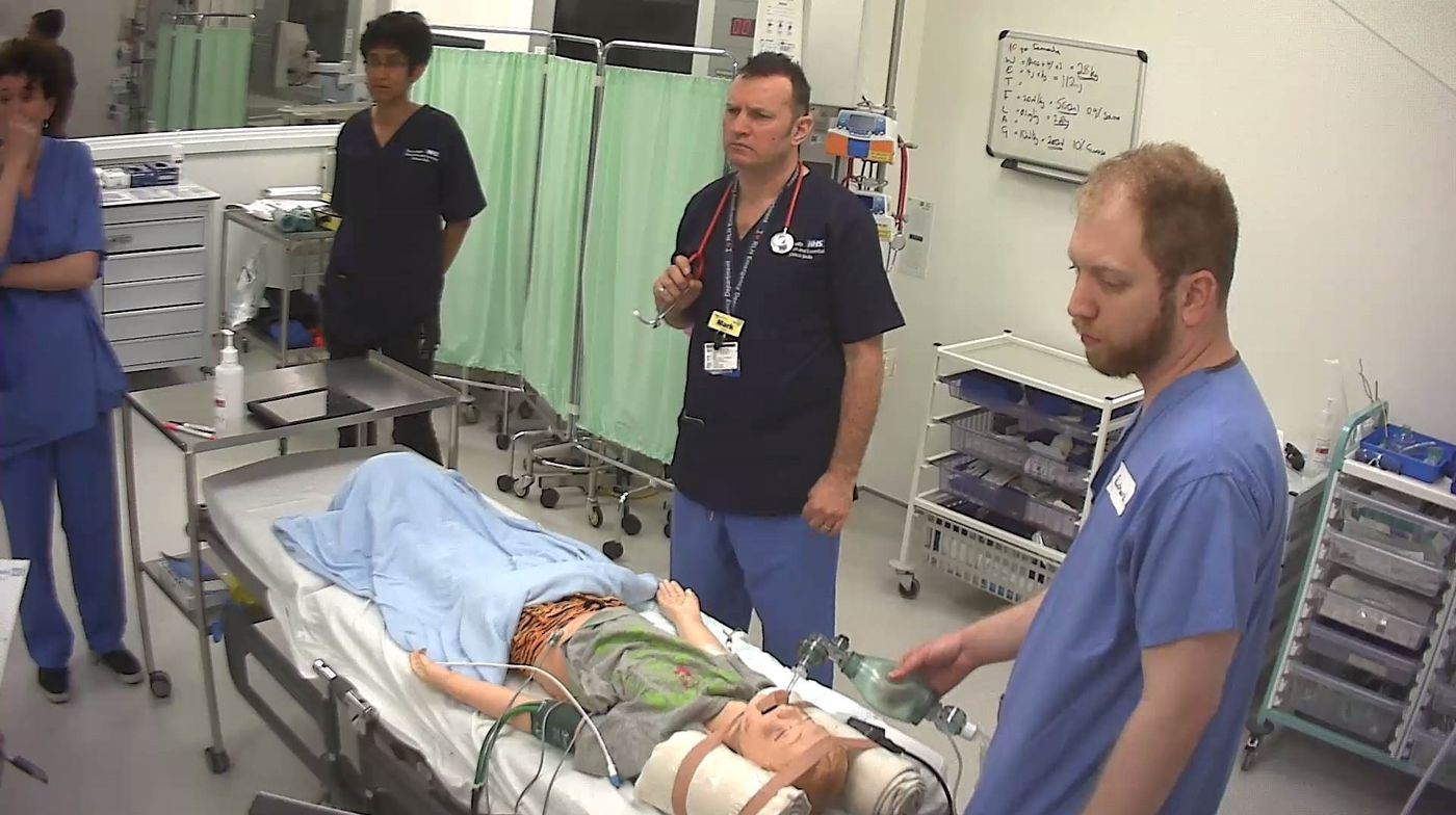 Delegates practising airway management on a paediatric manikin while faculty look on
